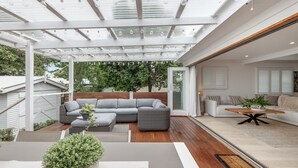 A modern patio with a glass ceiling, grey sofas, and a wooden coffee table. - Exquisite, Stunning & Central! CDB Fringe Cottage! (Toowoomba City)