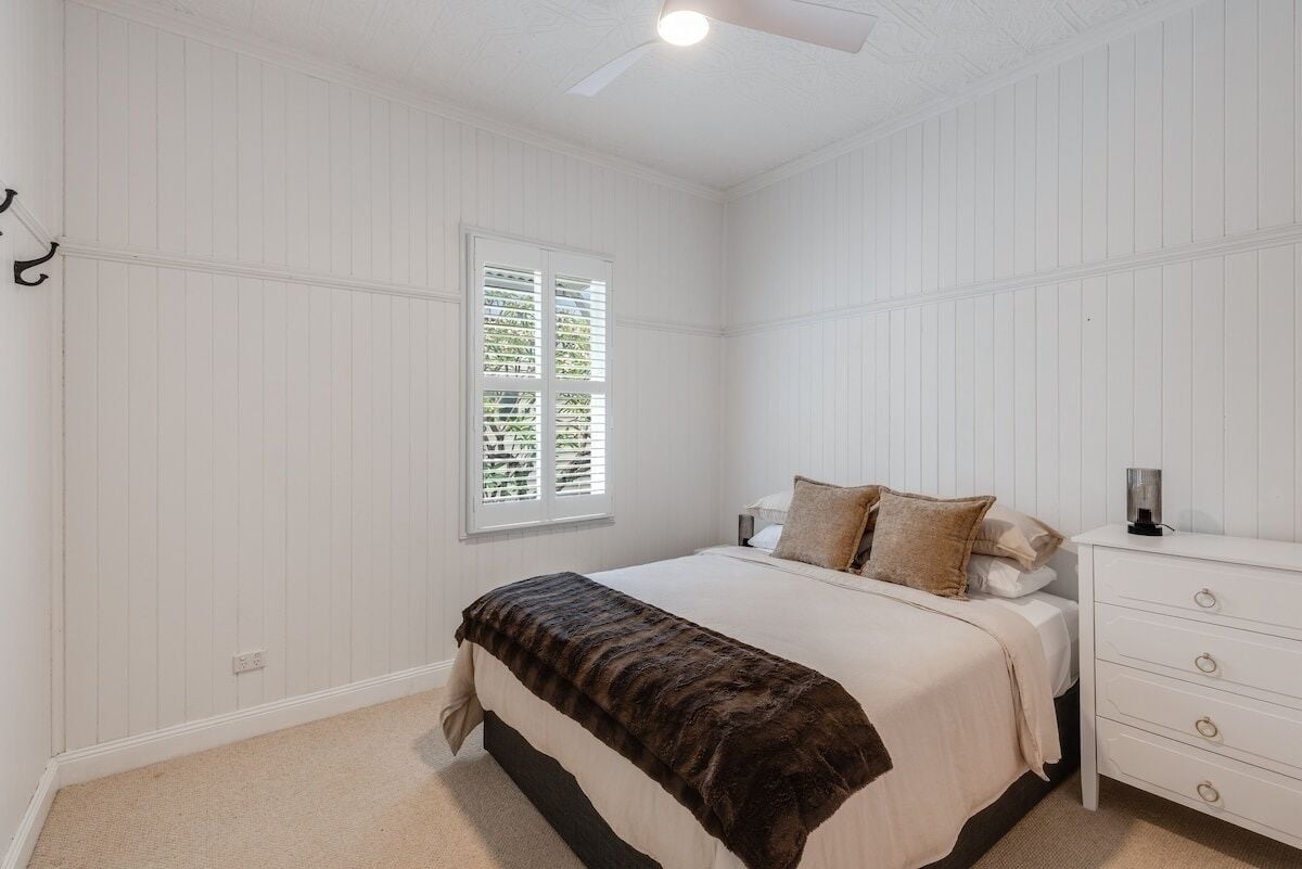 A bedroom with a bed, a nightstand, a window with blinds, and a ceiling fan.