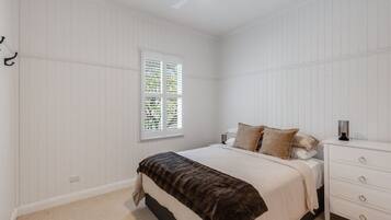 A bedroom with a bed, a nightstand, a window with blinds, and a ceiling fan.