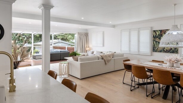 A spacious living area with a white sofa, a dining table with chairs, and a kitchen area with a white countertop and gold faucet. - Exquisite, Stunning & Central! CDB Fringe Cottage! (Toowoomba City)