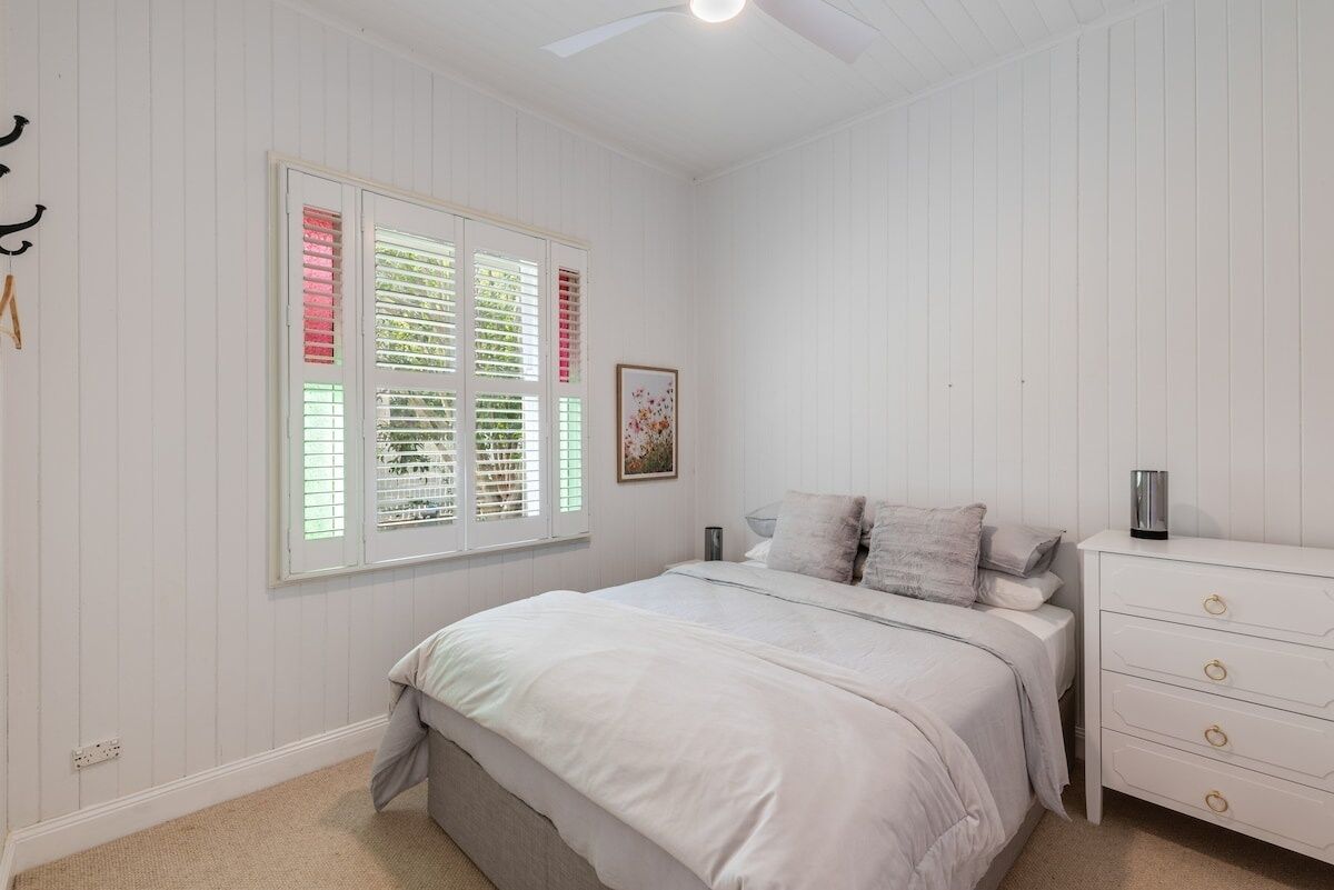 A bedroom with a bed, a dresser, a window with blinds, and a ceiling fan.