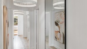 A hallway with white walls, wooden flooring, and a large mirror on the right. There are two large, white, woven light fixtures hanging from the ceiling. - Exquisite, Stunning & Central! CDB Fringe Cottage! (Toowoomba City)
