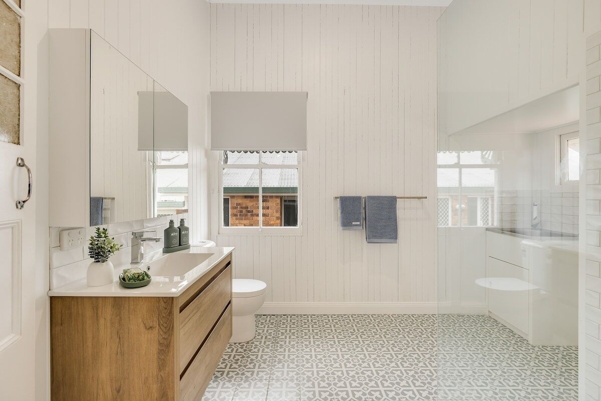 A modern bathroom with a wooden vanity, a large mirror, a toilet, and a window with a view of a brick building.