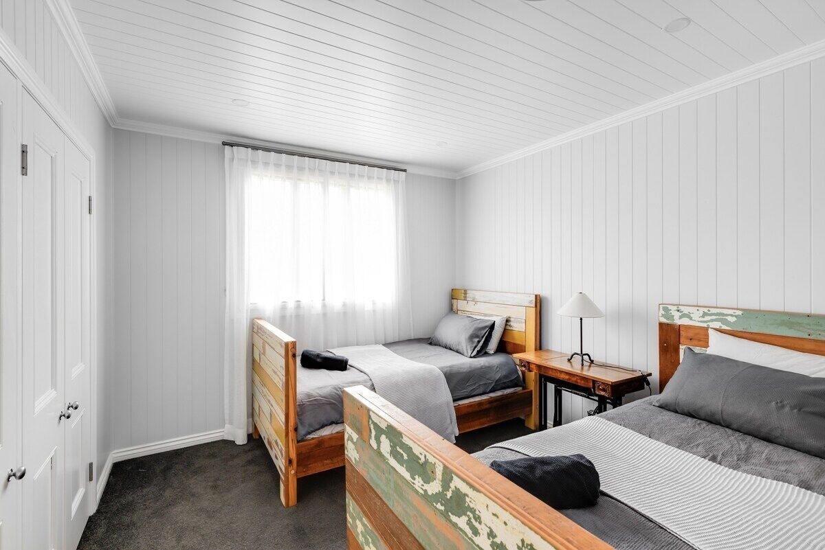 A room with two single beds, a small table with a lamp, and a wardrobe.