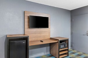 Una habitación de hotel moderna con televisión integrada, refrigerador pequeño y microondas.