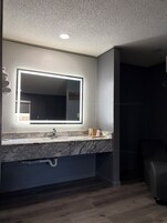 Un baño moderno con un espejo grande, un lavabo y una zona de ducha.