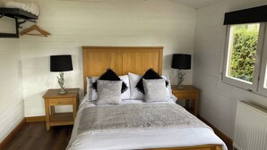 Une chambre à coucher avec un lit en bois, deux tables de chevet avec des lampes, un radiateur et une fenêtre donnant sur un paysage verdoyant.