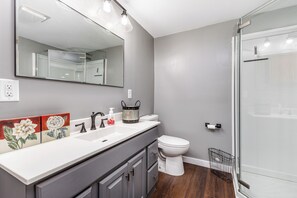 Features a large mirror above the vanity, a white sink, and a glass shower enclosure.