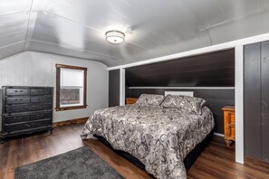 Relax in this serene bedroom with a large bed, dresser, and nightstand, set against a dark floor and headboard.