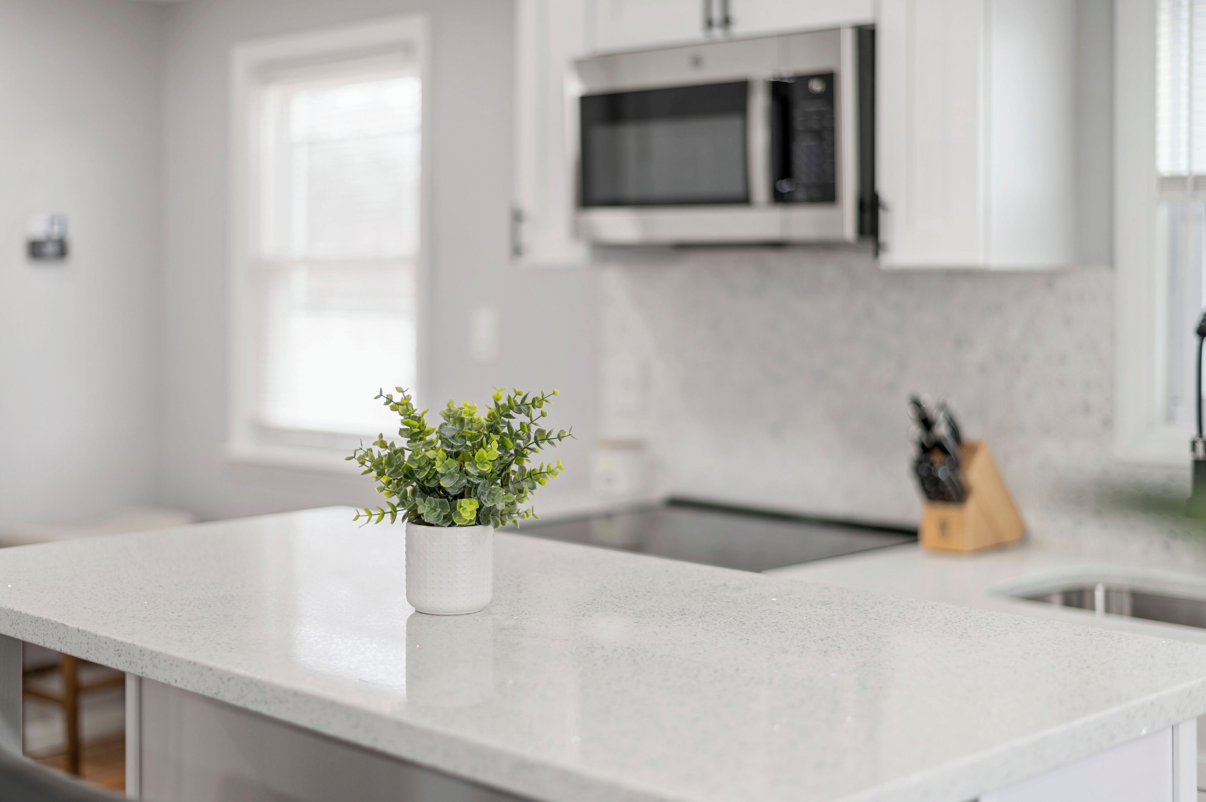 Una cocina moderna con armarios blancos, encimera blanca, microondas y bloque para cuchillos.
