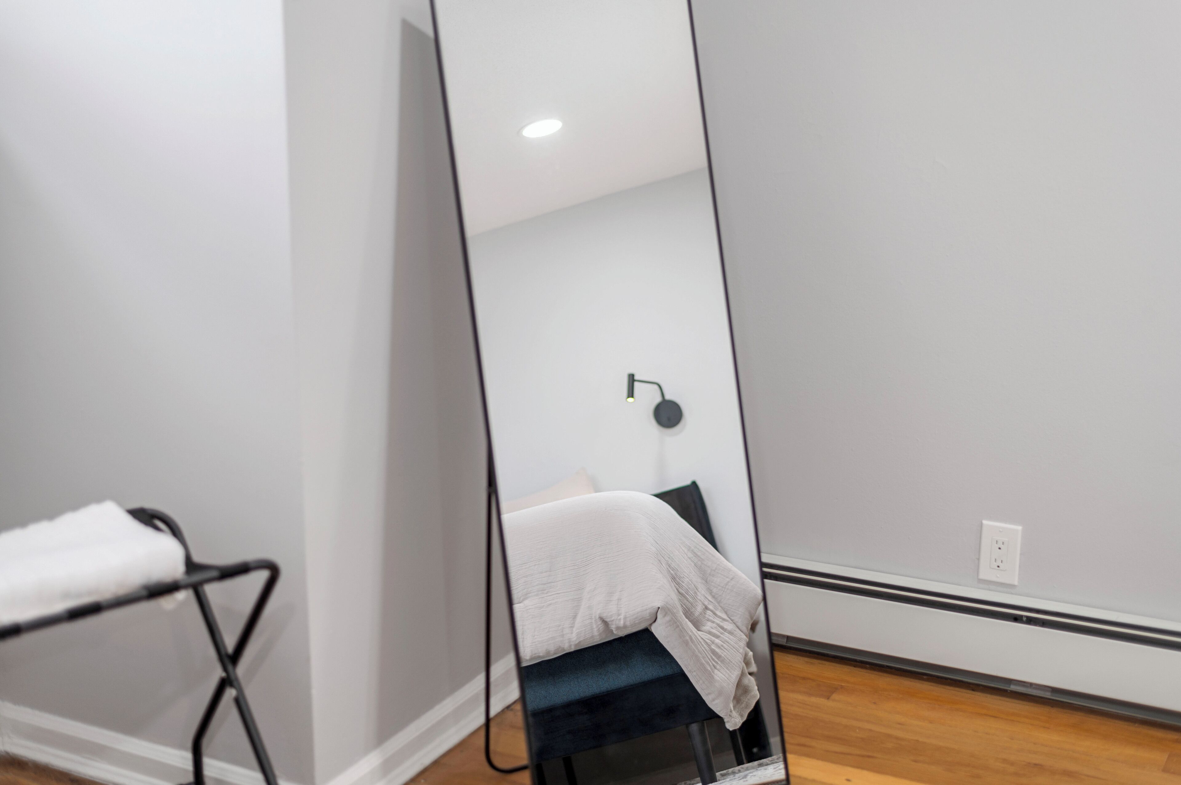 Un dormitorio moderno con un espejo grande, una cama con edredón blanco y una silla negra.