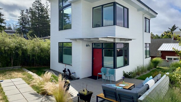 Ein modernes, zweistöckiges Haus mit einer Terrasse, ausgestattet mit Gartenmöbeln.
