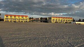 Ein Strandhotel mit mehreren gelben Gebäuden und roten Dächern, mit Balkonen und einem sandigen Strand im Vordergrund.