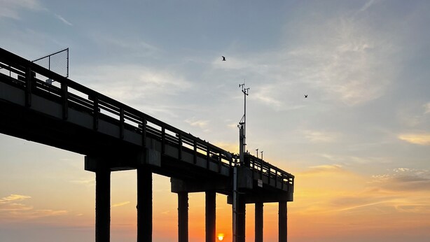 Ein Steg, der sich ins Meer erstreckt, mit einem Sonnenuntergang im Hintergrund.