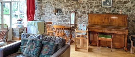 Una sala de estar acogedora con una pared de piedra, un piano, un sofá con cojines estampados y una zona de comedor con sillas de madera.