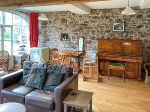 Una sala de estar acogedora con una pared de piedra, un piano, un sofá con cojines estampados y una zona de comedor con sillas de madera.