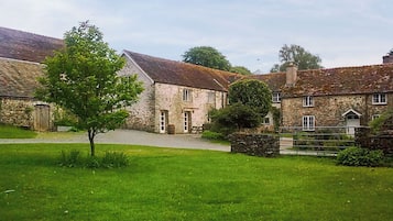 Un bâtiment en pierre avec une pelouse verdoyante et un arbre devant.