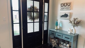 Une porte noire avec quatre fenêtres, une console bleu clair ornée de vases et d’une lampe à lave, et un mur sur lequel on peut voir une enseigne « Kentucky » et un tableau encadré.