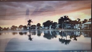 Ein ruhiger See spiegelt Bäume und Gebäude wider, über ihm strahlend blauer Himmel.