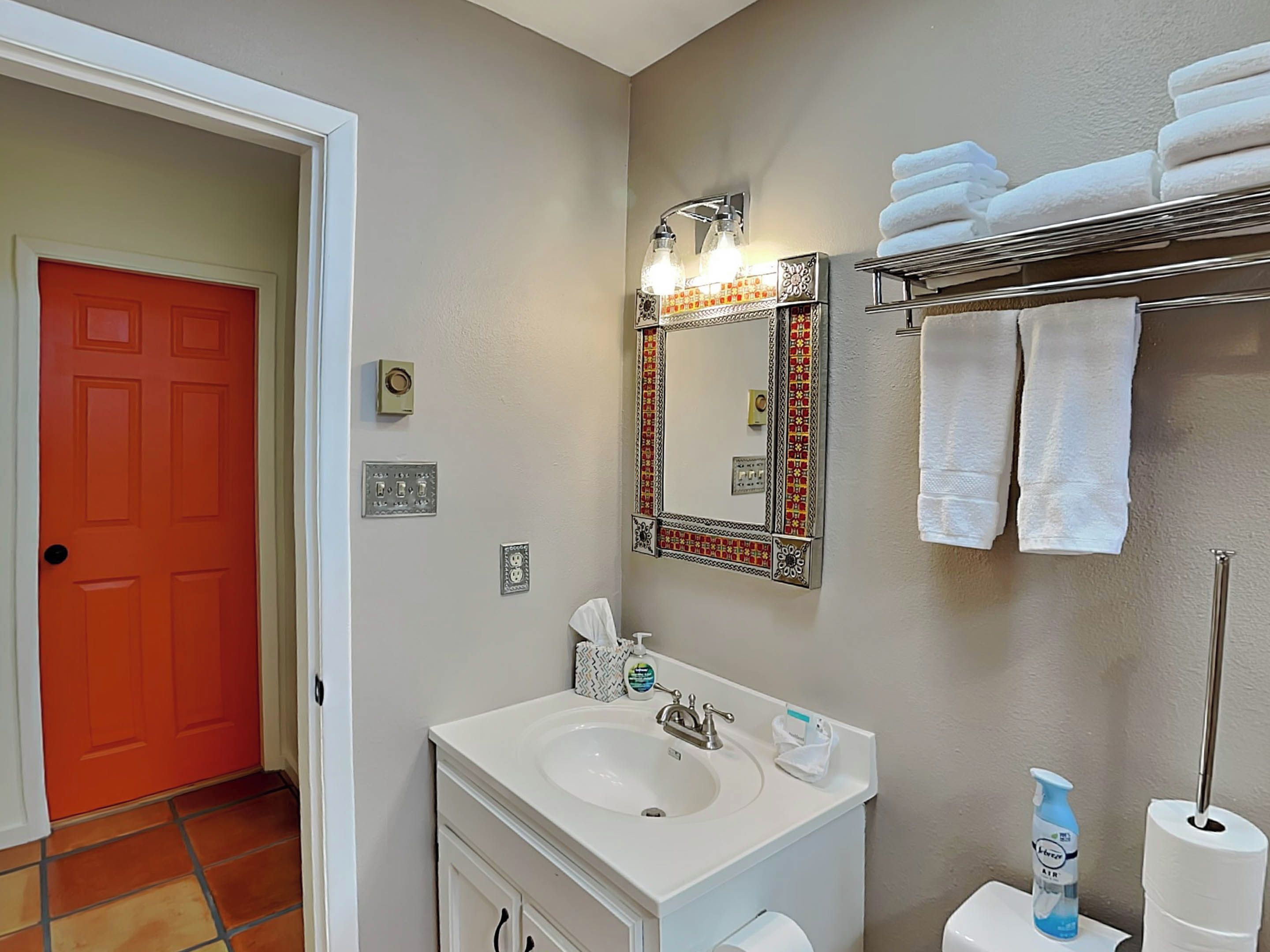 Un baño con un lavabo blanco, un espejo con marco decorativo, un perchero con toallas dobladas y una puerta roja.