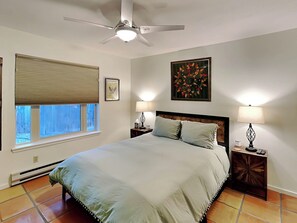 A bedroom with a bed, two bedside tables with lamps, a ceiling fan, a window with blinds, and a wall-mounted artwork. - Casa Calabaza by Kokopelli Property Management (Santa Fe)