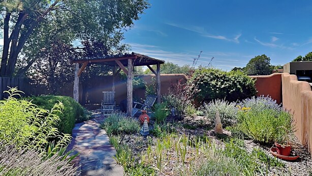 Un giardino con un pergolato in legno, un vialetto lastricato e diverse piante e fiori.