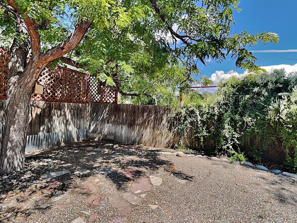 A gravel pathway leading to a wooden fence with a lattice design, surrounded by trees and a clear sky. - Casa Calabaza by Kokopelli Property Management (Santa Fe)