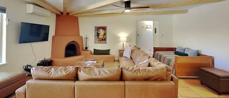 A spacious living room with a large leather sofa, a fireplace, a television, and a ceiling fan.