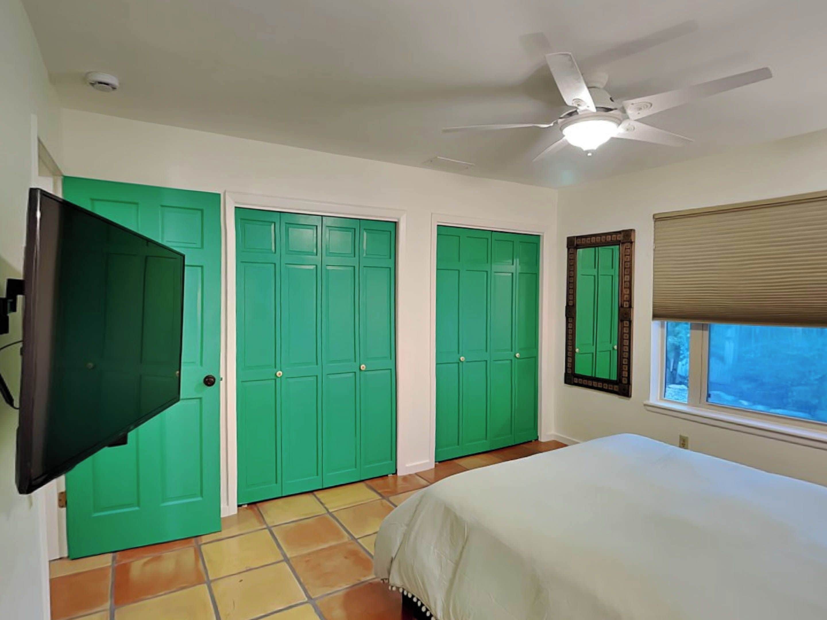 A bedroom with a bed, a ceiling fan, and green doors.
