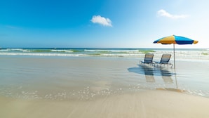 Een strand met twee ligbedden onder een blauwe en gele parasol.