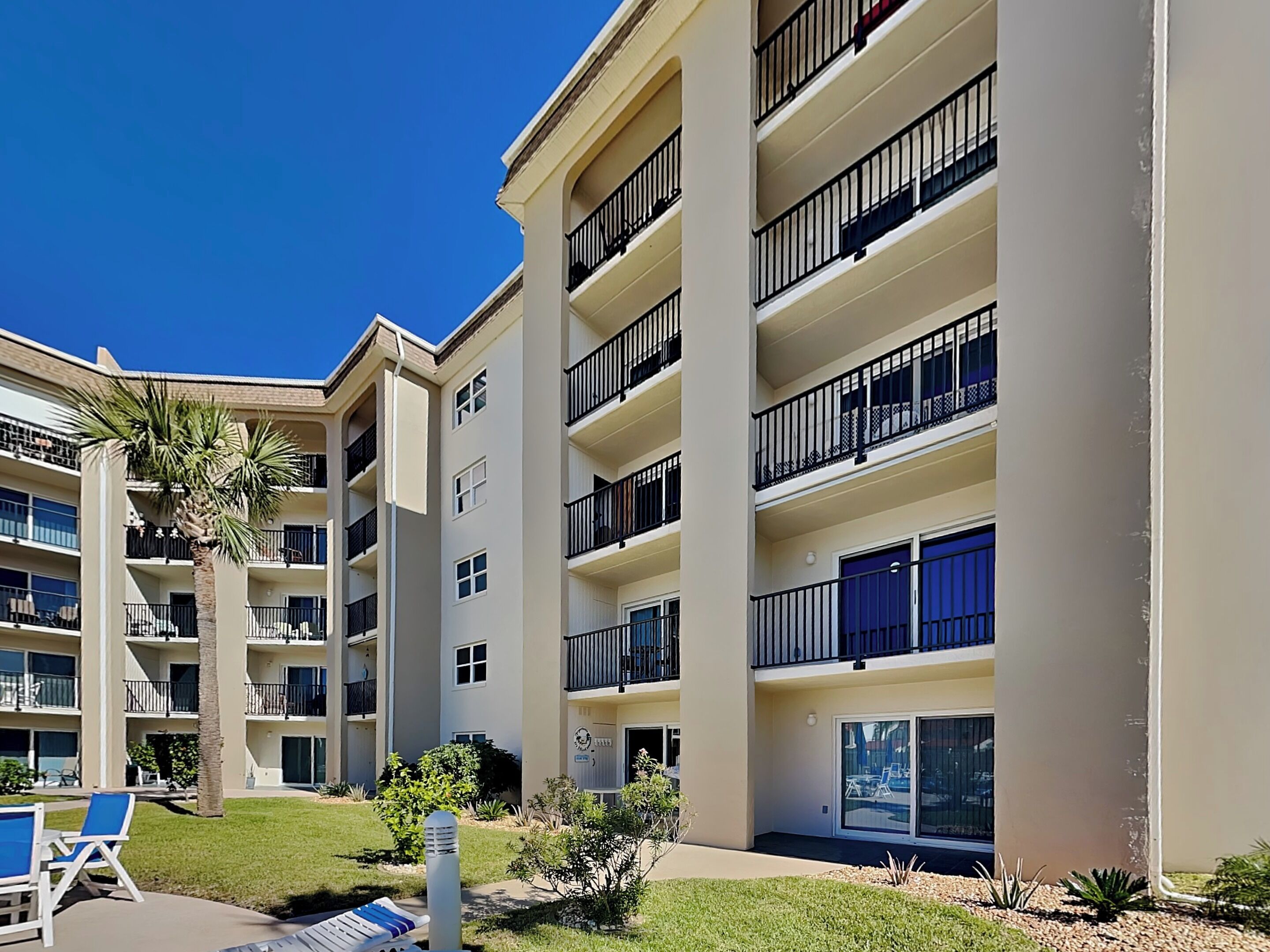 Um edifício residencial com vários andares, varandas, piscina e um jardim bem cuidado.