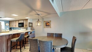 Een moderne keuken met een centraal eiland, een eethoek met een ronde tafel en stoelen, en een plafond met inbouwspots.