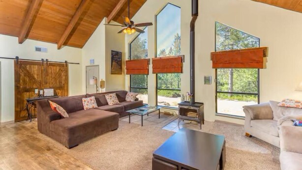 A spacious living area with a high ceiling, a fireplace, and large windows offering views of the outdoors. - Cody's Comfy Cabin-Near Yosemite (Mariposa)