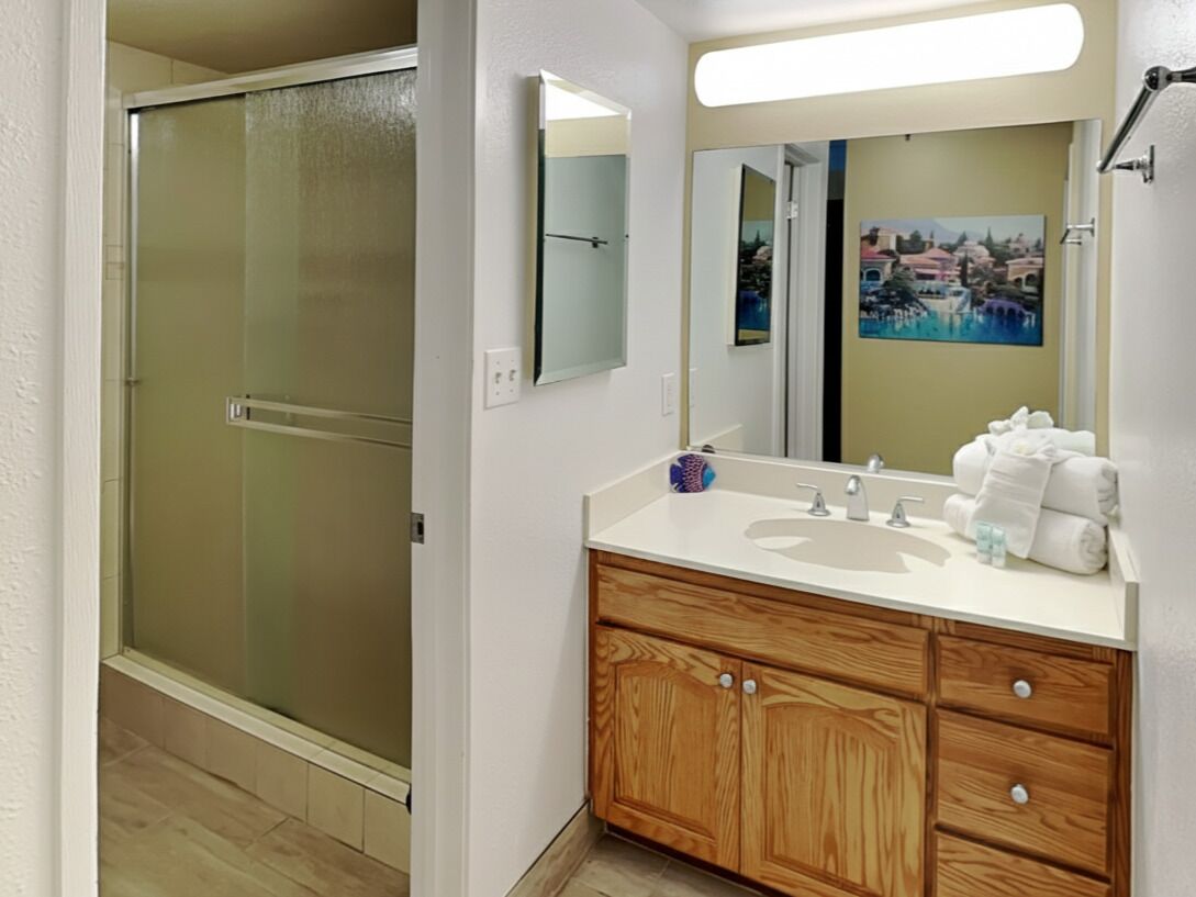 A bathroom with a glass shower door, a wooden vanity with a sink, and a mirror.