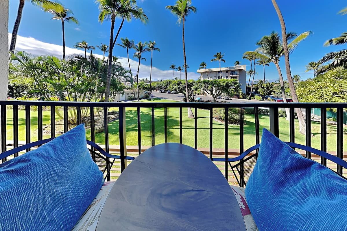 A balcony with a view of a lawn, palm trees, and a building in the background.