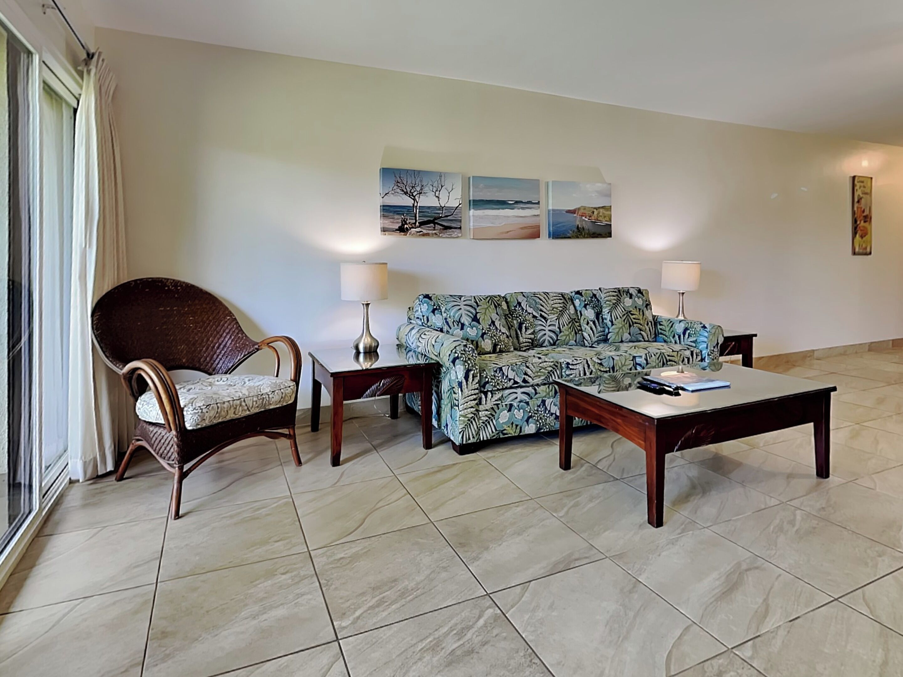 A living room with a sofa, armchair, coffee table, and two lamps. There are three paintings on the wall.