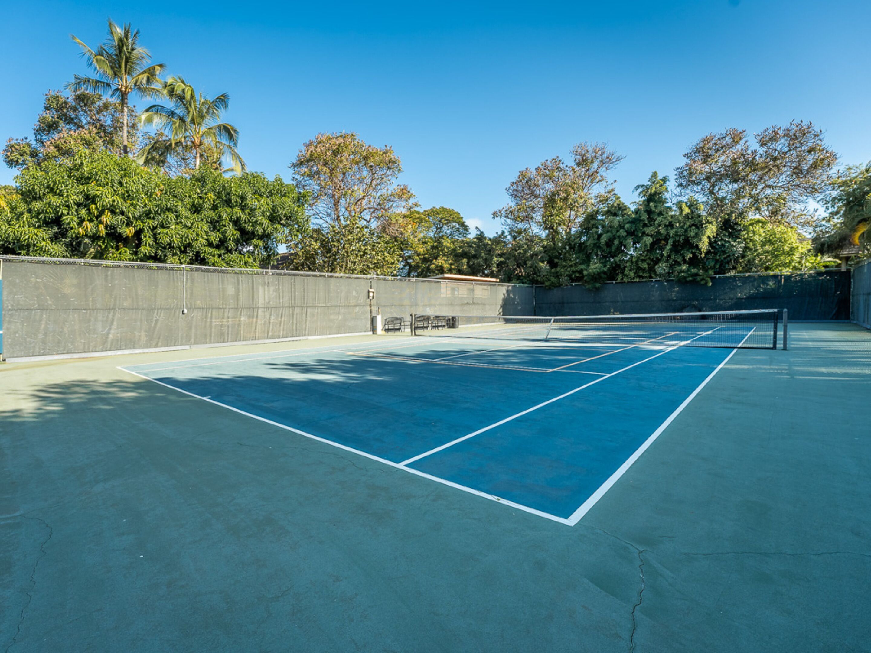 A tennis court with a net, surrounded by a concrete wall and trees.