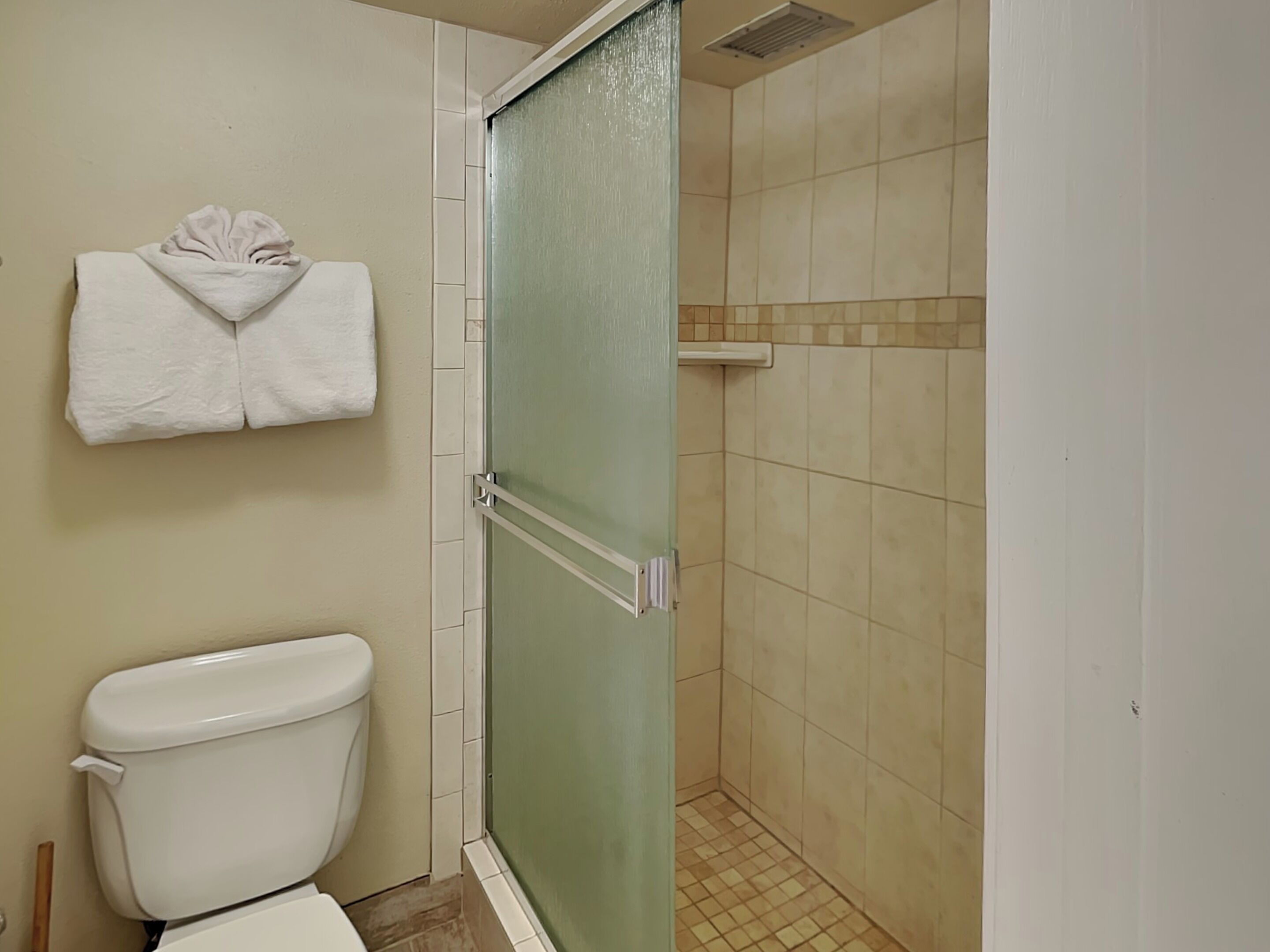 Un baño con inodoro, ducha con puerta de cristal y toalla colgada en la pared.