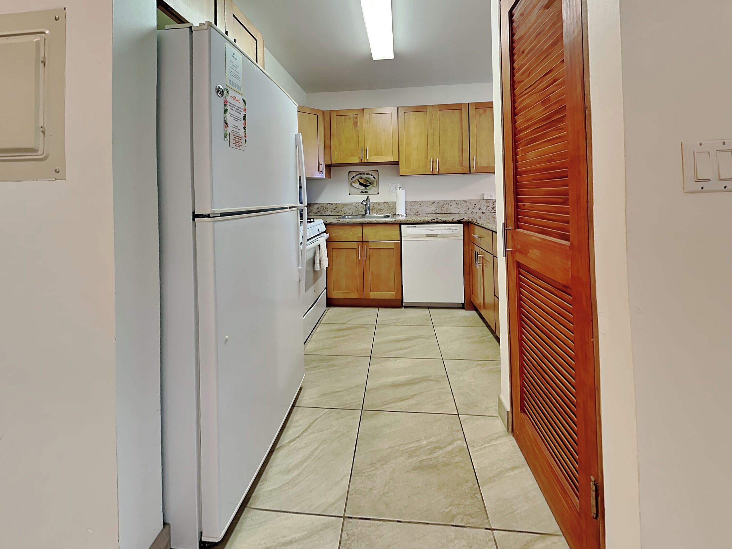 A narrow kitchen with wooden cabinets, a white refrigerator, and a dishwasher.