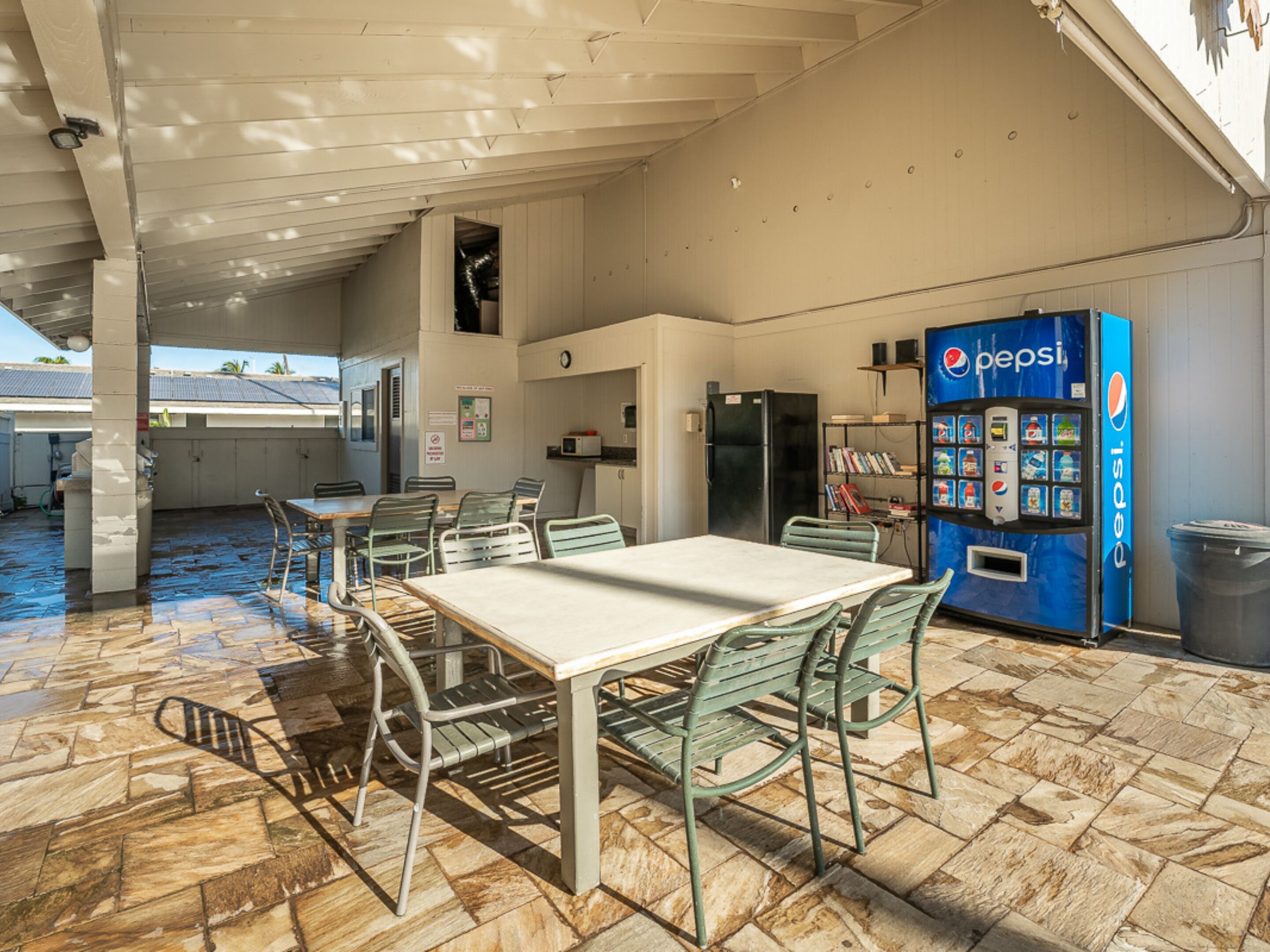 Un espace de restauration intérieur comprenant une table et des chaises, un réfrigérateur, un four à micro-ondes et un distributeur automatique de boissons Pepsi.
