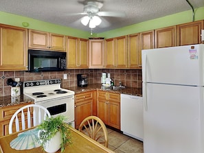 A kitchen with wooden cabinets, a microwave, stove, refrigerator, and a ceiling fan.