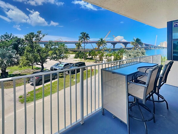 A balcony with a view of a bridge, palm trees, and parked cars. - Lovers Key Beach Club by Distinctive Beach Rentals (Fort Myers Beach)