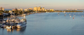 Un port de plaisance où sont amarrés de nombreux bateaux, avec la silhouette d’une ville en arrière-plan et un pont qui enjambe l’eau.