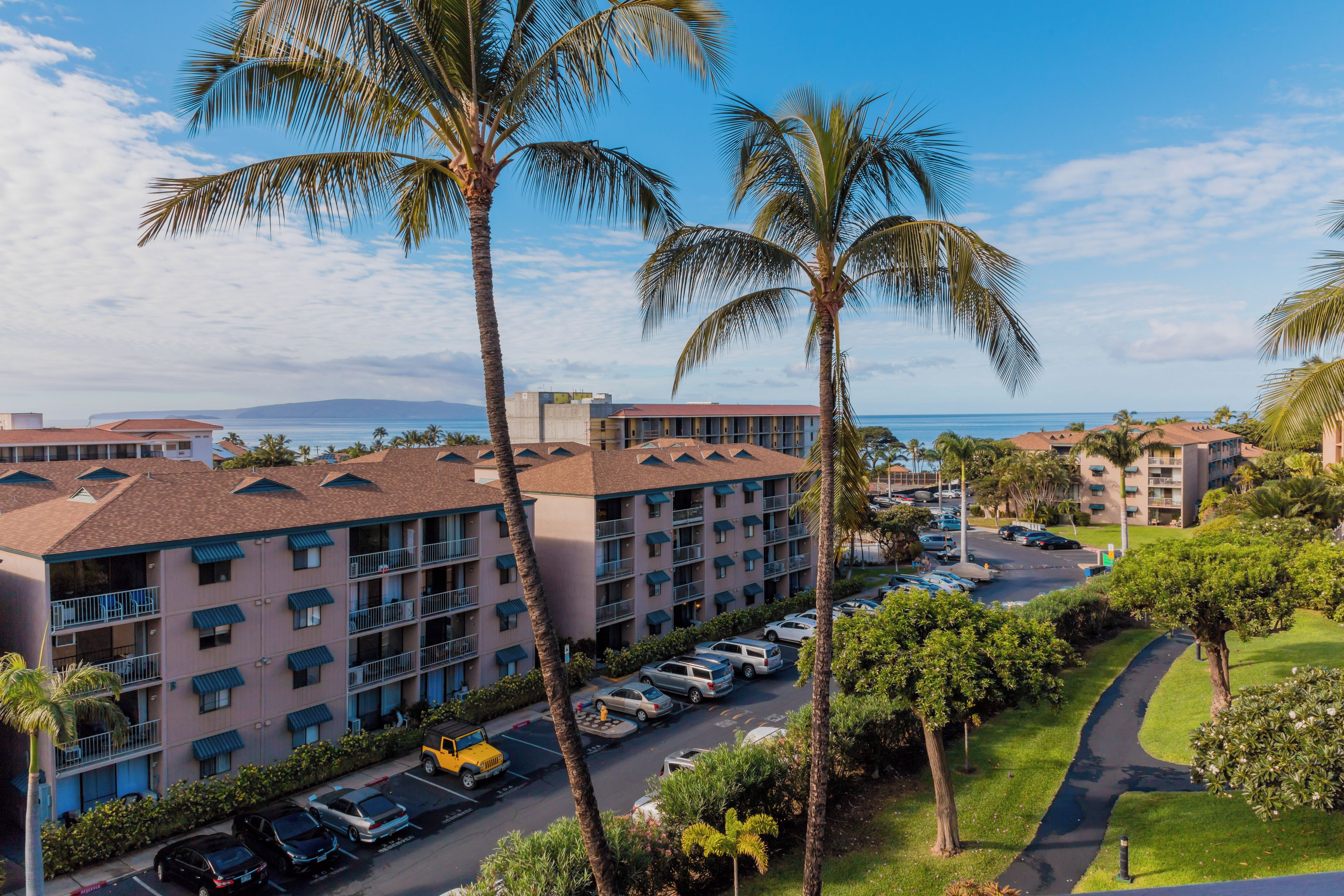 A multi-story hotel with balconies, a parking lot, and a view of the ocean.