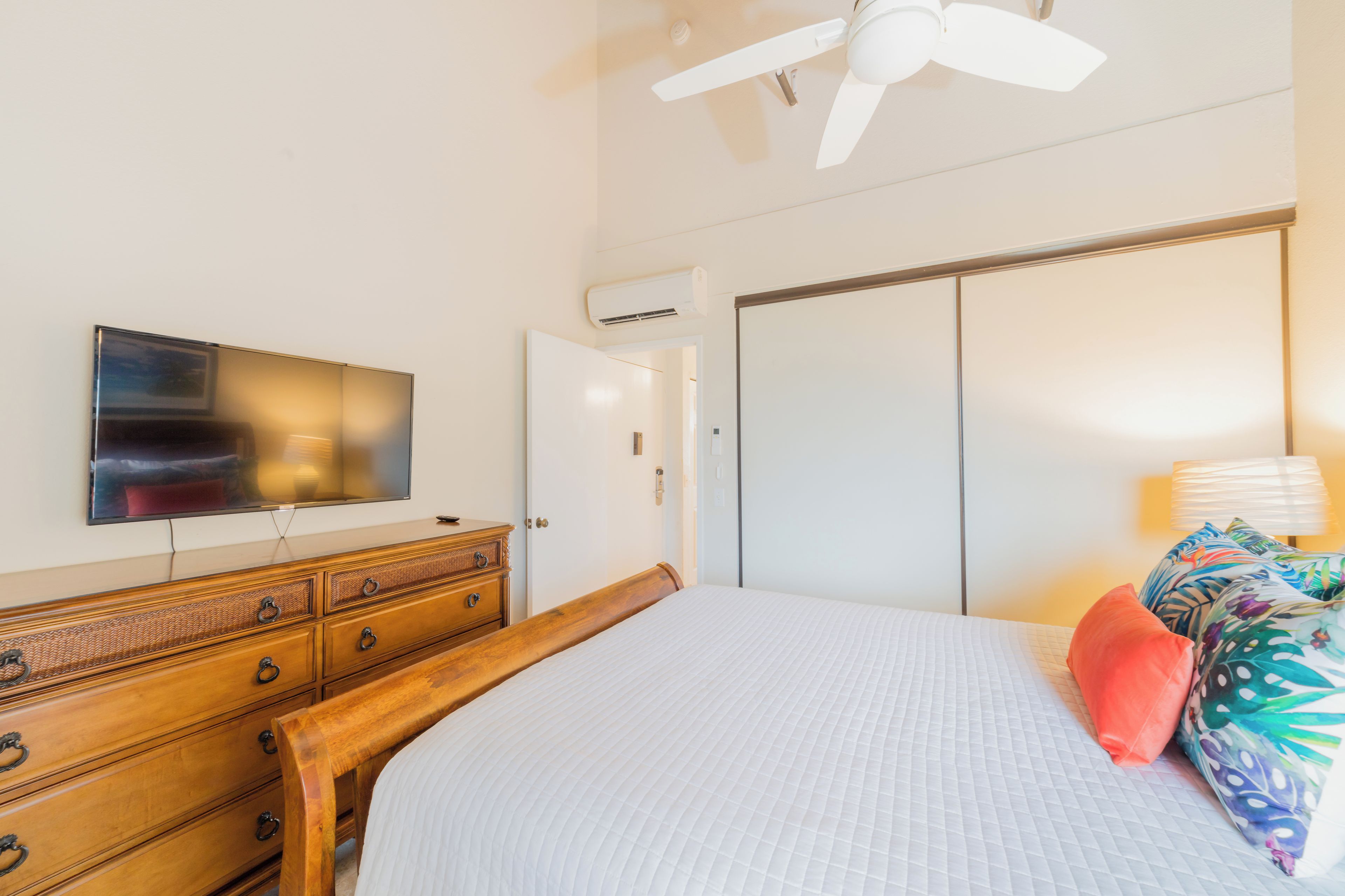 Ein Schlafzimmer mit einem Bett, einer hölzernen Kommode, einem Fernseher, einem Kleiderschrank und einem Deckenventilator.