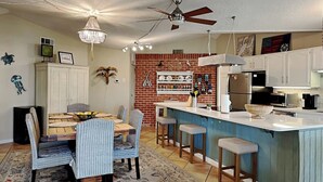 A kitchen with a brick backsplash, white cabinets, a bar area with stools, and a chandelier. - Siesta Keys by Miss Kitty’s (Rockport)