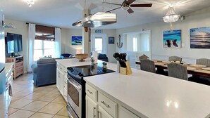 A spacious kitchen with white cabinetry, a large island, and a dining area with a table and chairs. - Siesta Keys by Miss Kitty’s (Rockport)