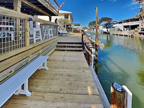 A wooden dock extending over a body of water with a bench and a railing. - Siesta Keys by Miss Kitty’s (Rockport)