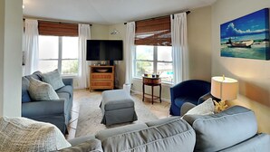 A living room with a sofa, ottoman, TV, and a painting on the wall. - Siesta Keys by Miss Kitty’s (Rockport)