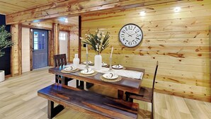 Une salle à manger en bois avec une grande table dressée pour quatre personnes, une horloge au mur et une porte au fond.